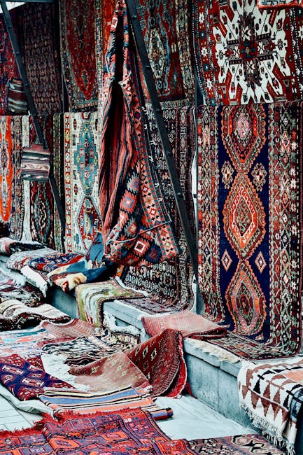 A variety of intricately patterned and colorful Persian-style carpets displayed on a long table at Nag Head Market in N7, with some carpets showing ornate designs in gold, black, green, and beige tone